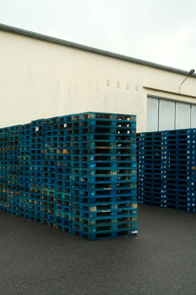 pexels photo 10096887 10096887 High stacks of blue plastic pallets outside a warehouse building.